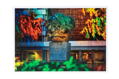 Postkarte mit Foto: Große steinerne Büste von Karl Marx vor einem Gebäude, umgeben von buntem Herbstlaub in Rot, Grün und Gelb